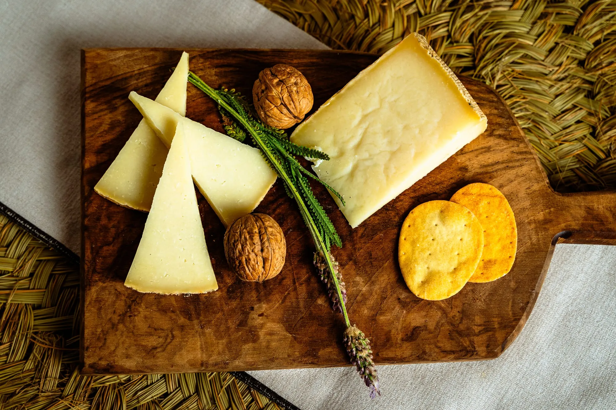 Tabla de queso manchego con cuñas, nueces, lavanda y crackers sobre esparto