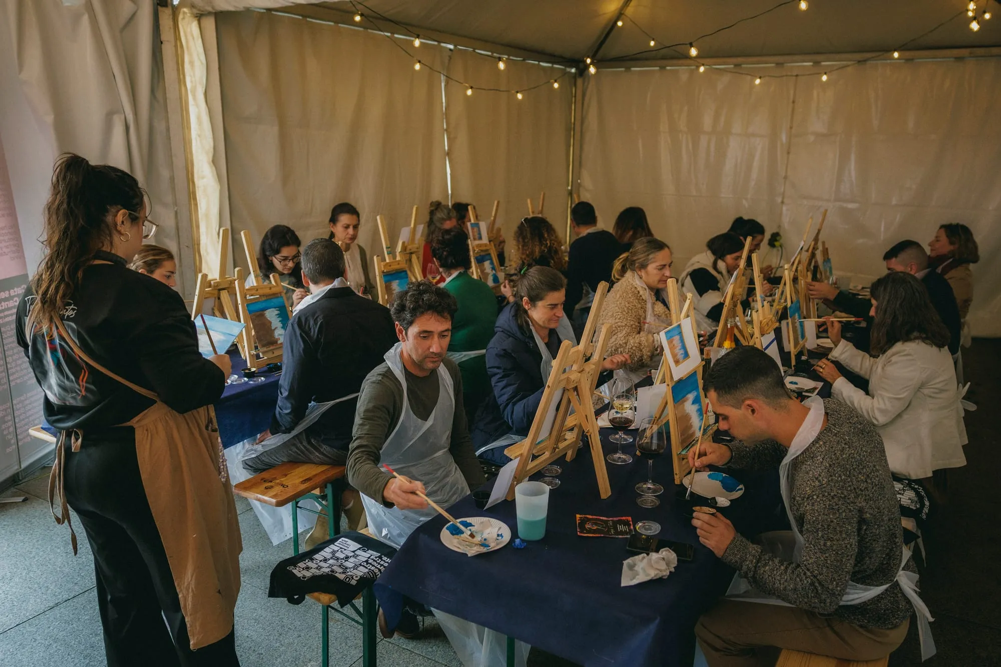 Taller Trazos y Tintos en la carpa: participantes pintando en caballetes con una copa de vino