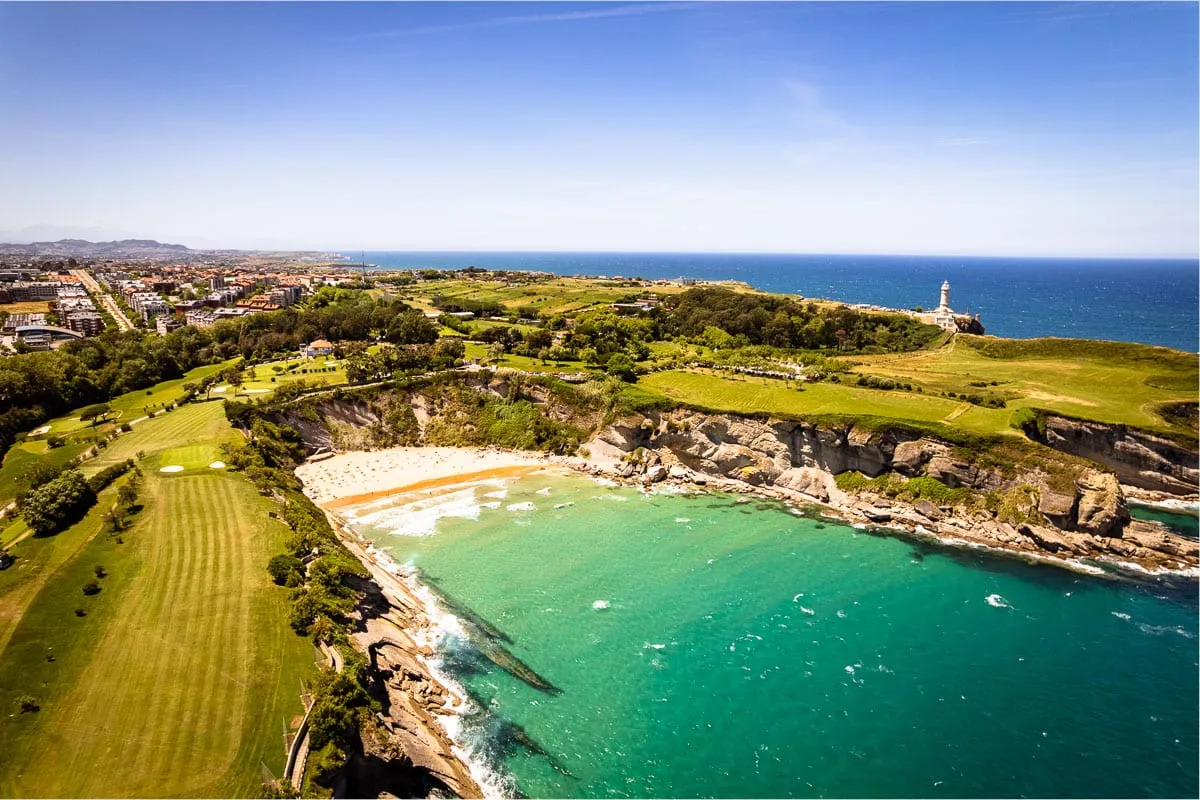 Cala de Mataleñas desde el aire, con el agua turquesa, el campo de golf y el faro de Cabo Mayor
