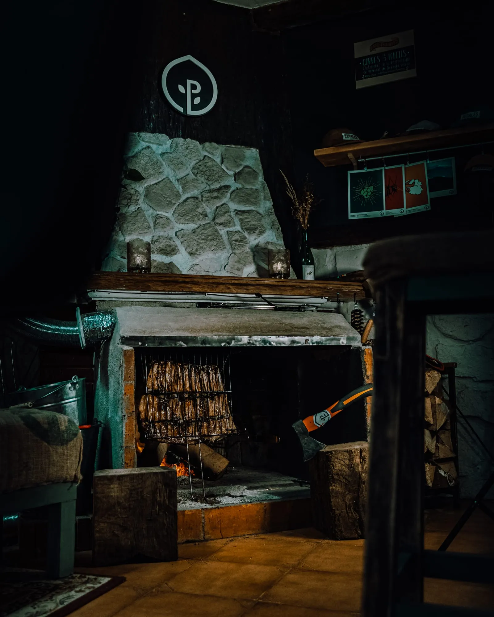Chimenea de piedra con parrilla encendida, hacha y el logotipo de Pedales sobre la campana