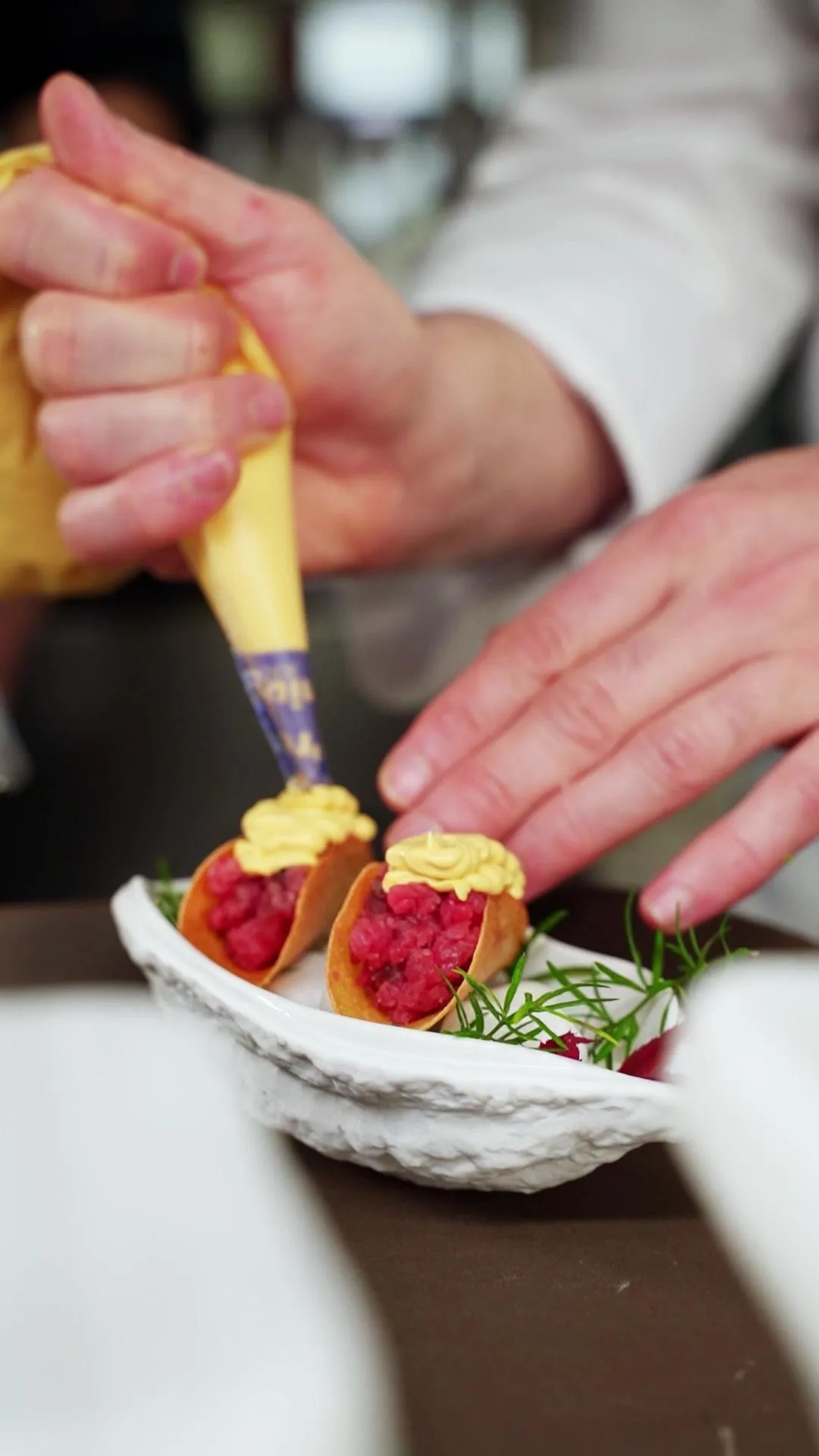 Manos de un cocinero terminando dos bocados de tartar con manga pastelera
