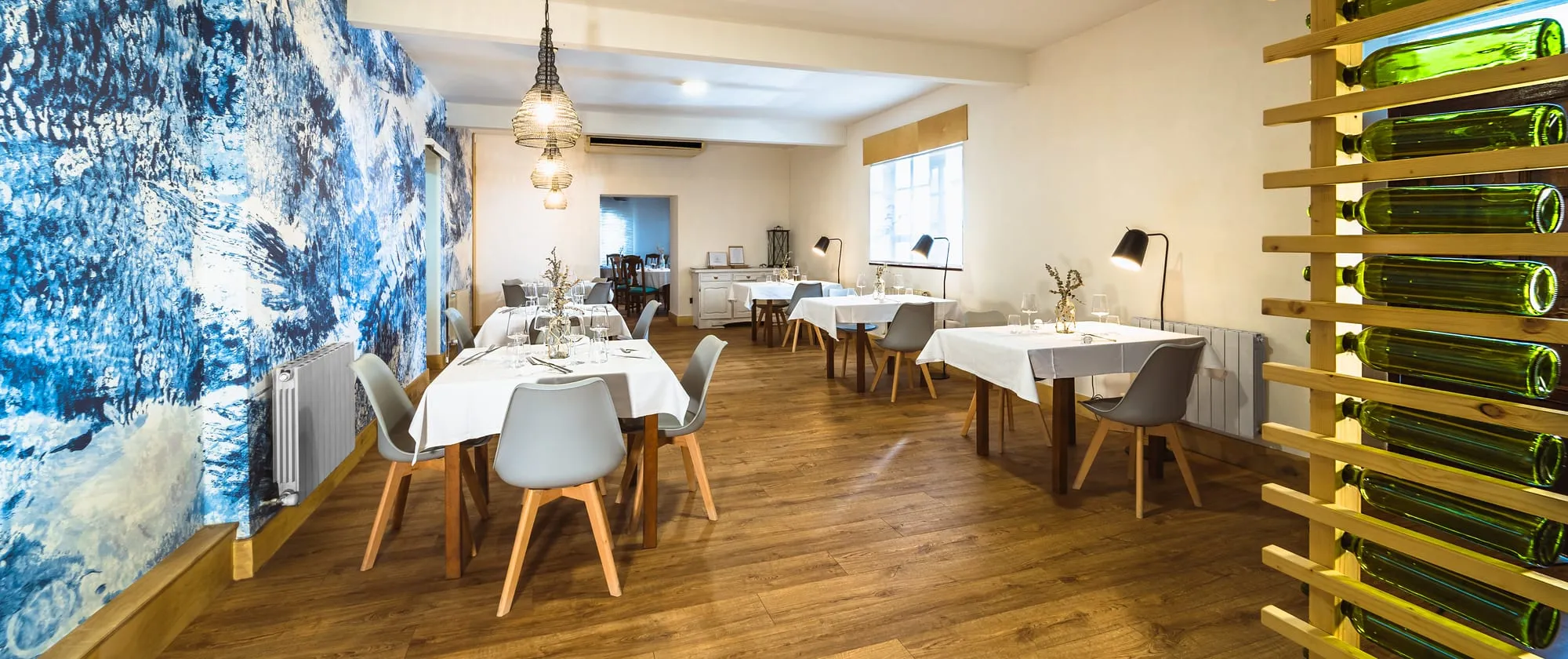 Comedor del Restaurante César con mesas vestidas de blanco, sillas nórdicas y mural azul