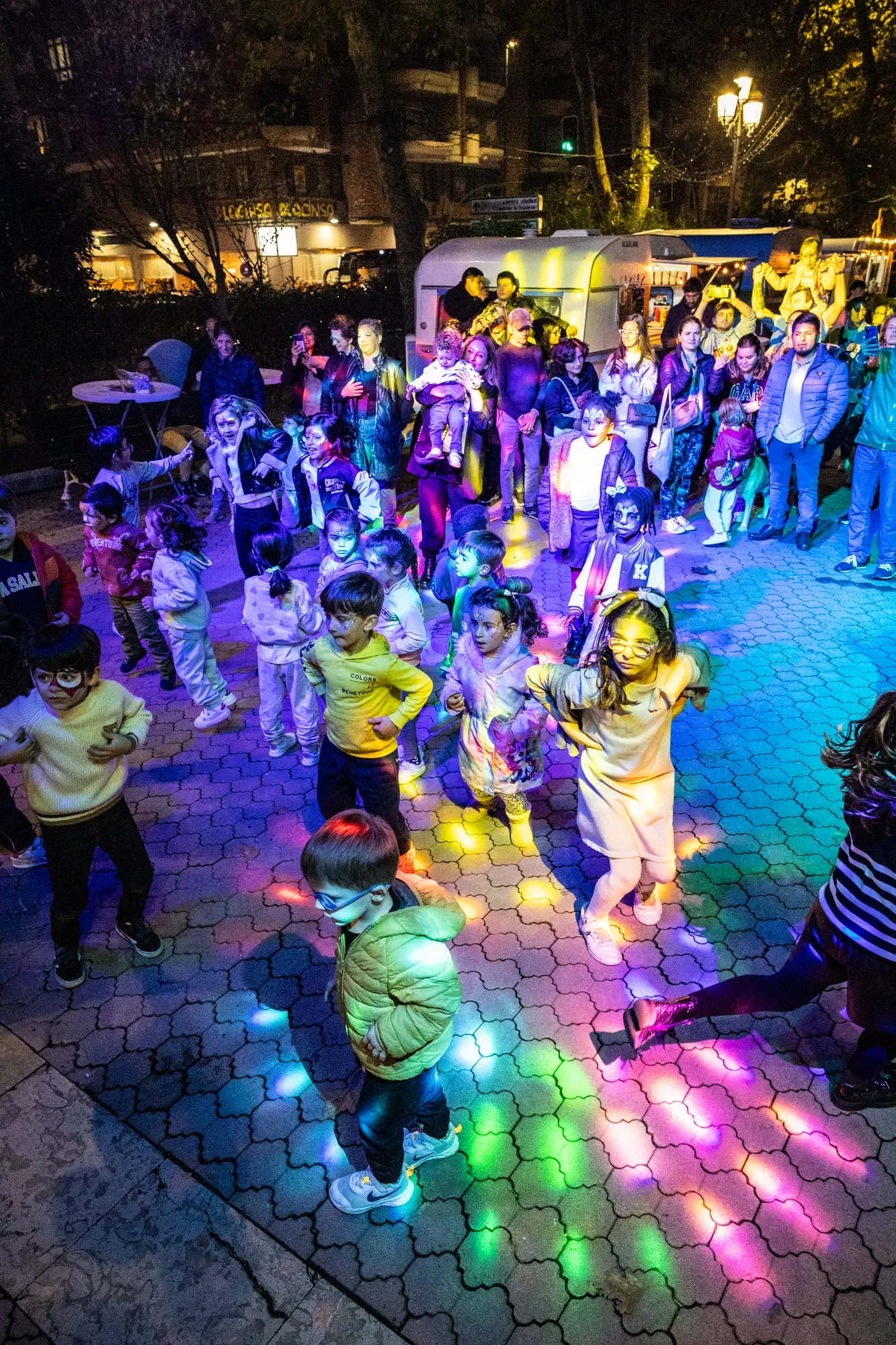 Público bailando de noche sobre una pista de luces de colores en la fiesta del comercio local