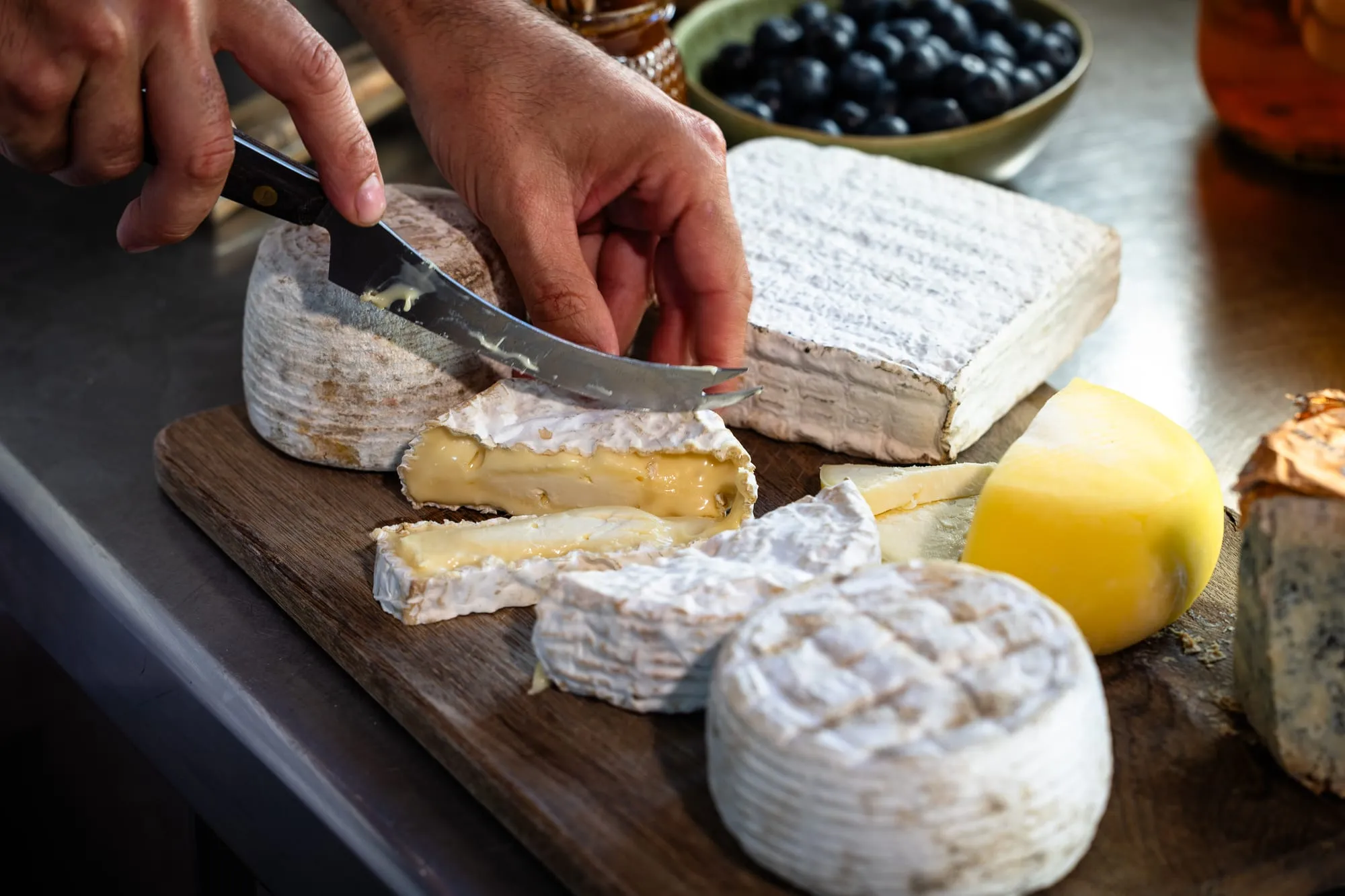 Primer plano de una tabla de quesos cántabros con cuchillo, arándanos y un queso curado