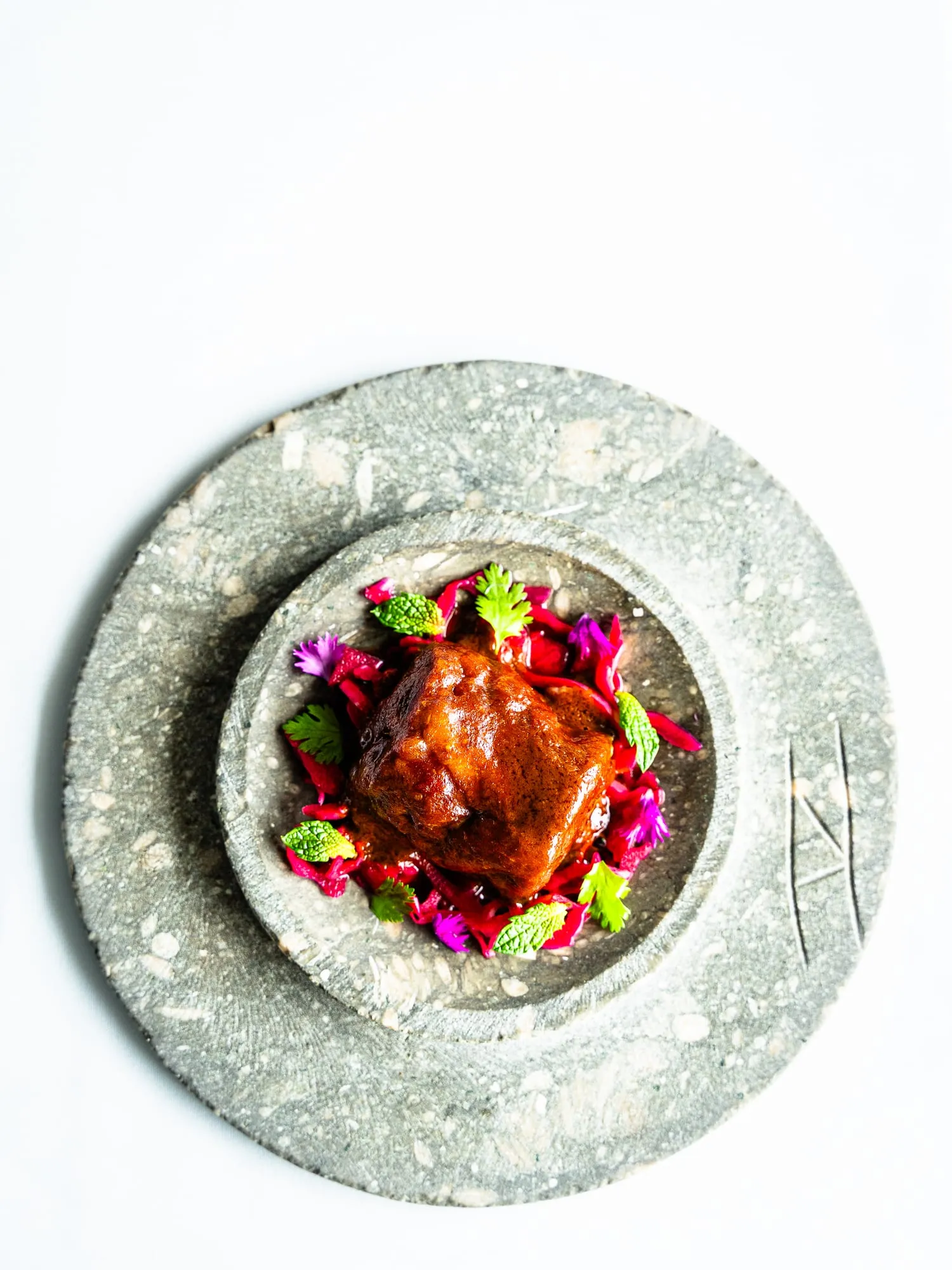 Carne glaseada sobre lombarda morada y brotes verdes en un plato de piedra gris con el sello de Emma
