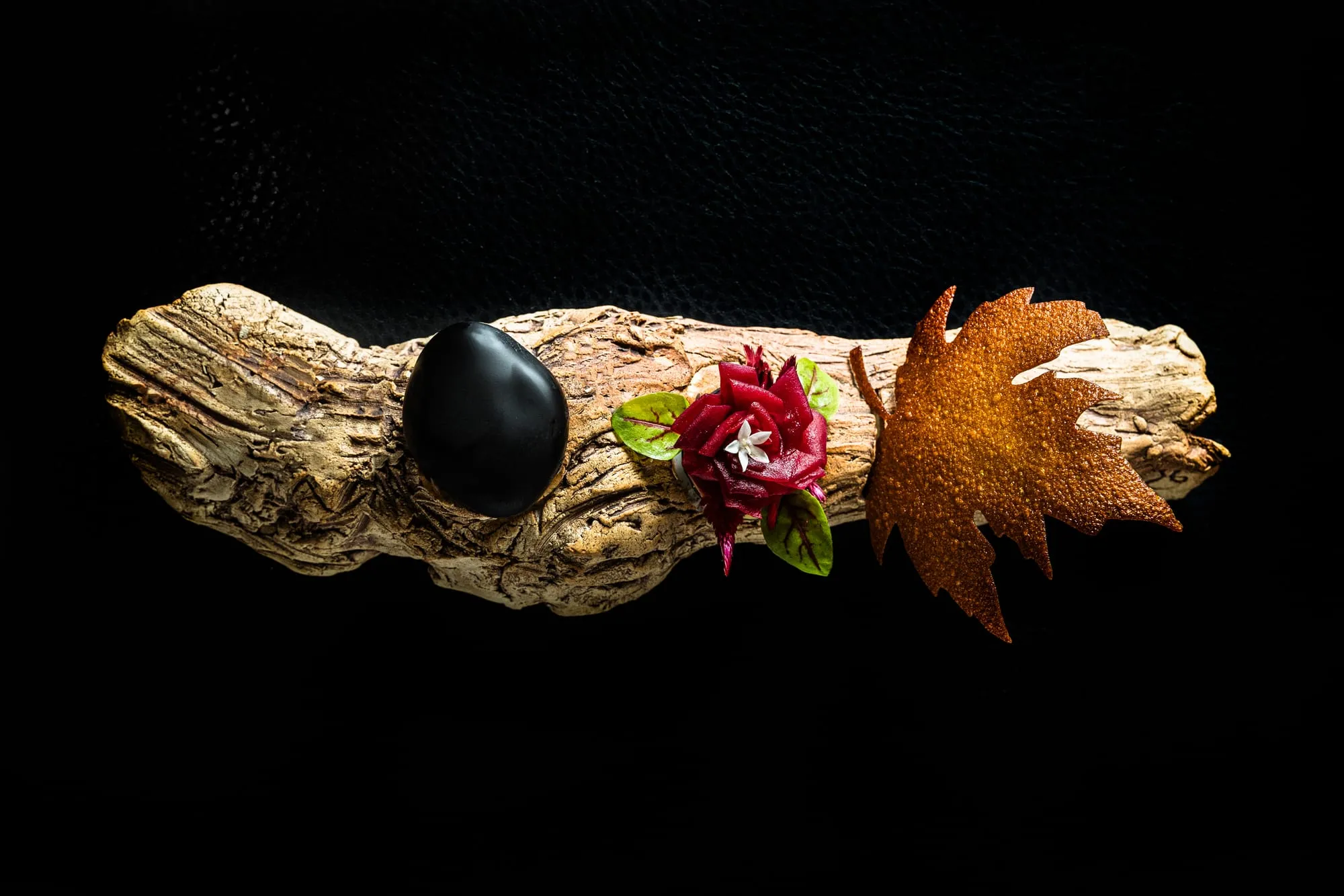 Aperitivos sobre un tronco de madera con una piedra negra, una flor y una hoja crujiente