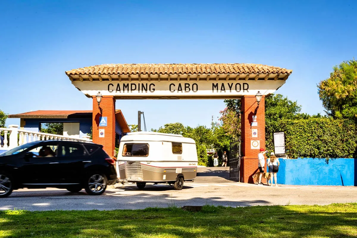 Arco de entrada de madera con el rótulo Camping Cabo Mayor y una caravana pasando