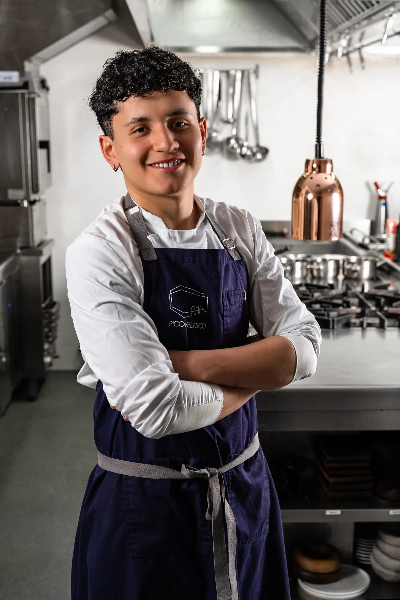 Cocinero joven con delantal y brazos cruzados, sonriendo en la cocina del restaurante