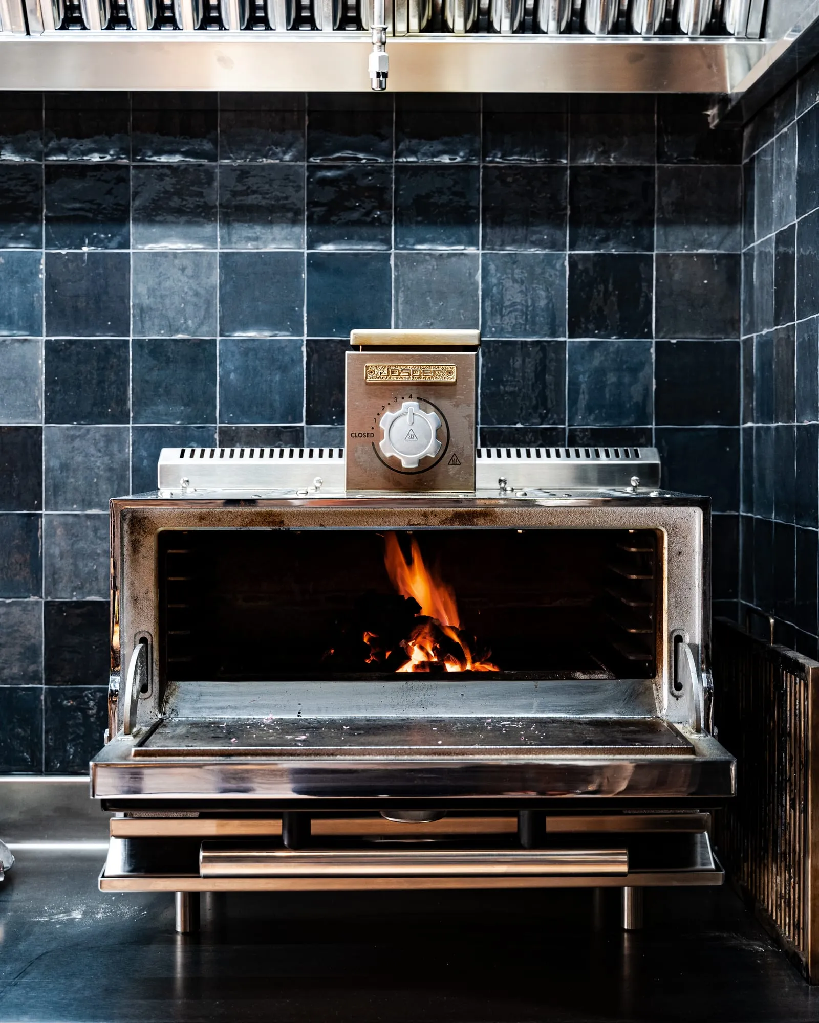 Horno de brasas encendido entre azulejos azul oscuro en la cocina del restaurante