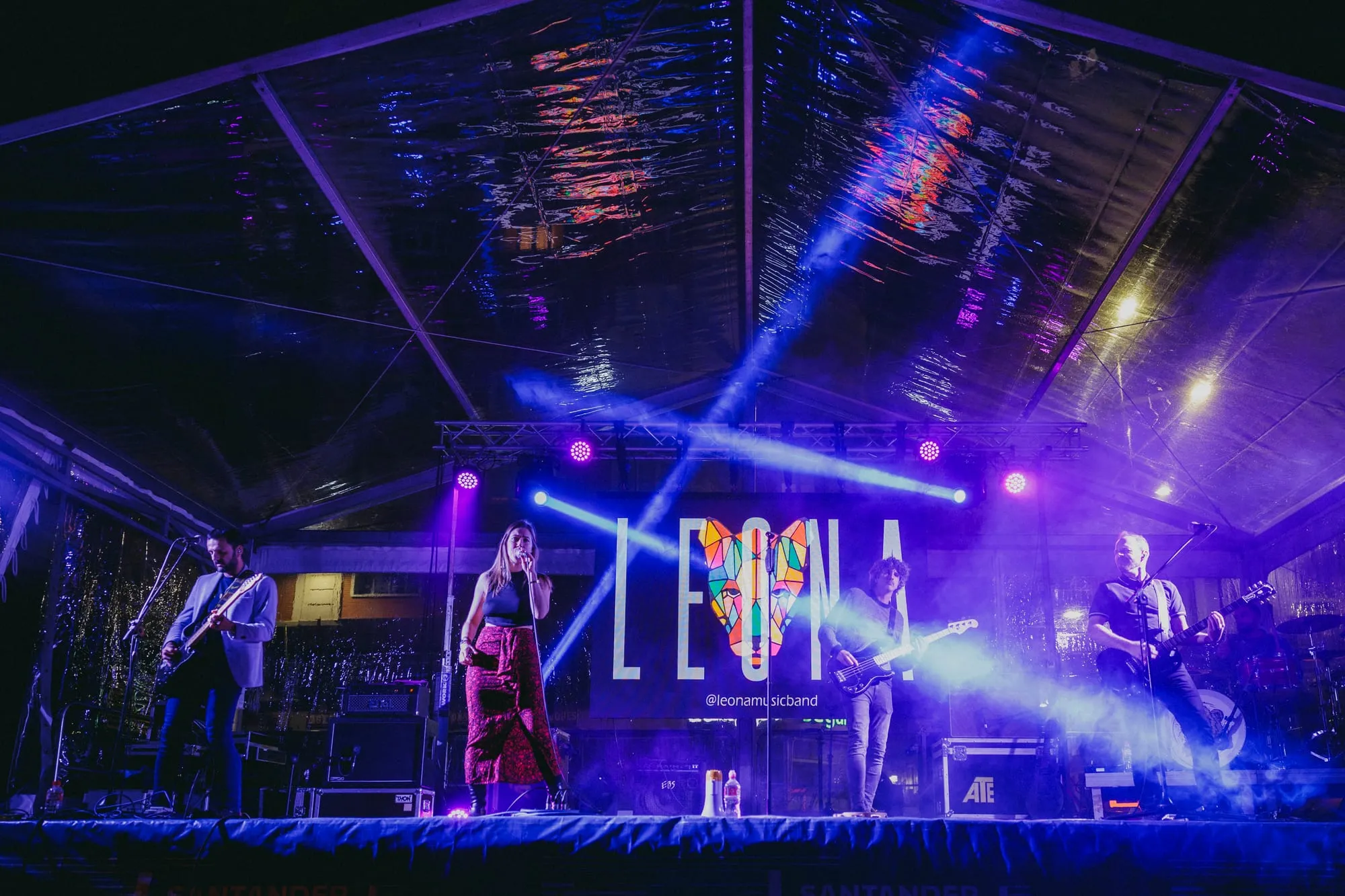 Leona en directo en el escenario del festival con el nombre del grupo en la pantalla y luces moradas