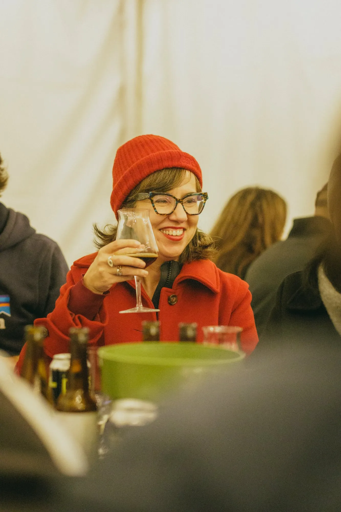 Una chica con gorro rojo sonríe y brinda con una copa de vino en una mesa de la carpa