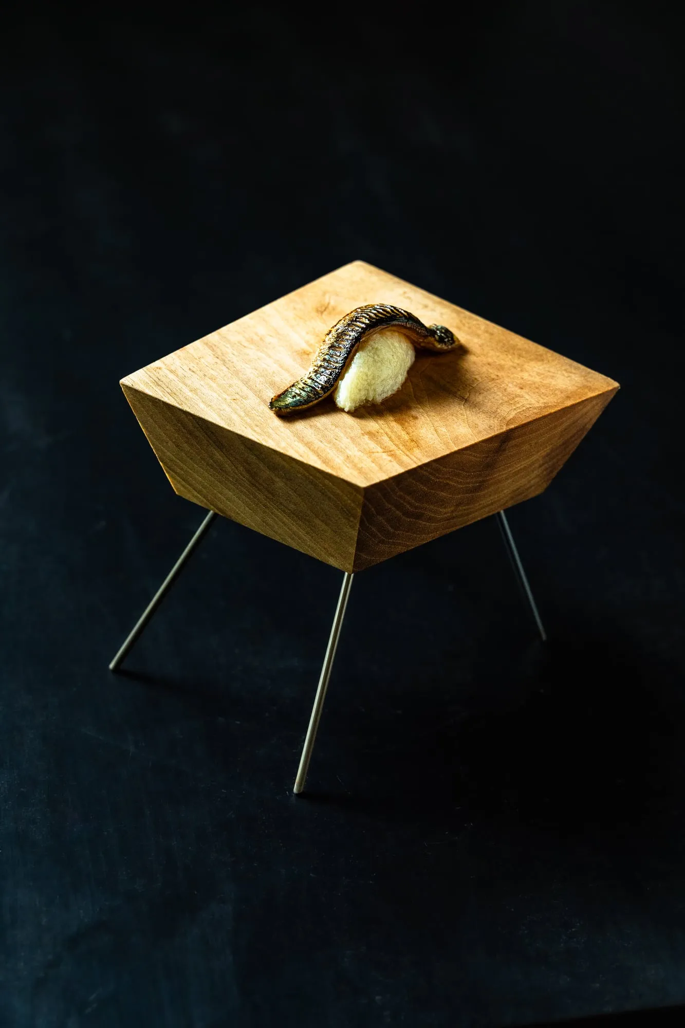 Bocado del menú servido sobre una pieza de madera facetada con patas, sobre fondo oscuro