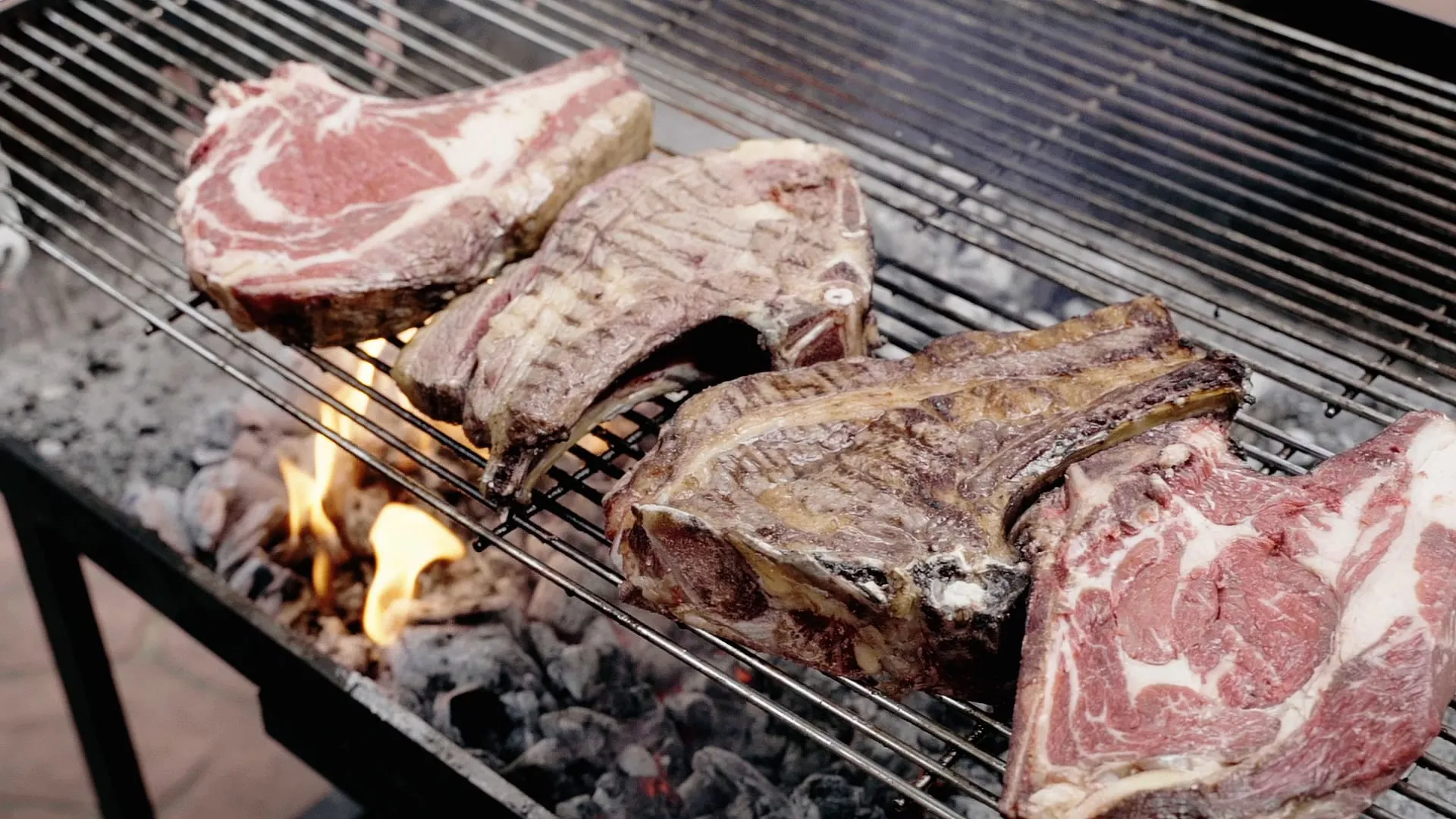 Chuletas de vaca sobre la parrilla de carbón con llamas por debajo, en la cocina exterior del encuentro